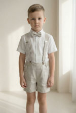 Boy wearing a beige linen suspender shorts set with white short-sleeve shirt and bow tie, minimalist lifestyle look.