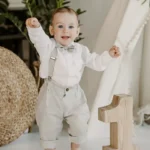 Baby boy in beige linen suspender pants with white shirt and bow tie, front view