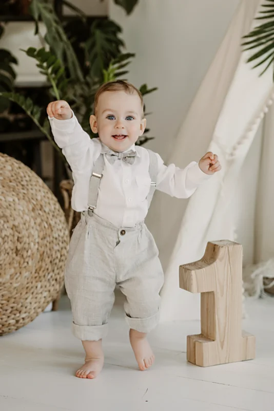 Baby boy in beige linen suspender pants with white shirt and bow tie, front view