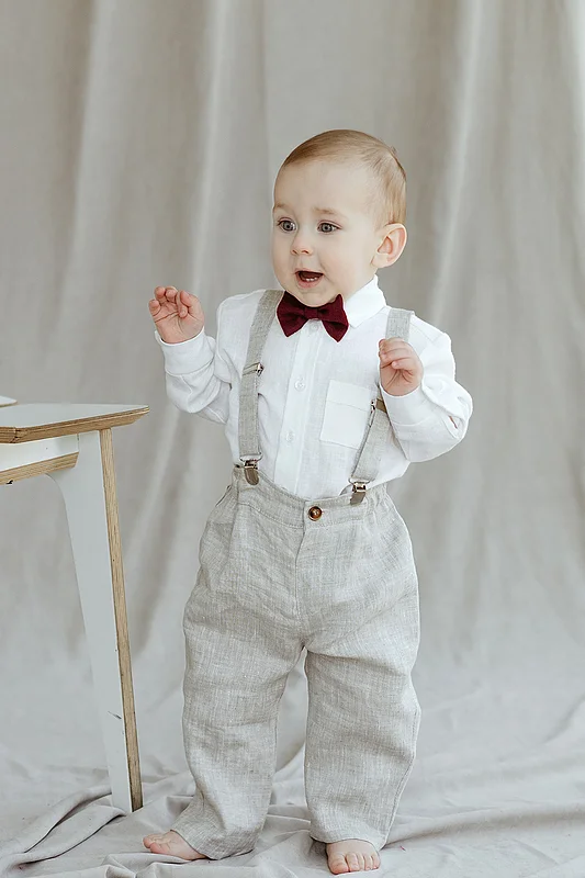 Baby boy in beige linen suspender pants with white shirt and bow tie, front view