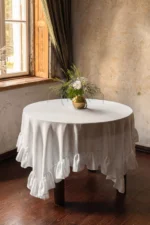 Square white linen overlay placed on a round table over a base tablecloth